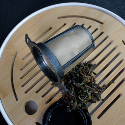 Black & Gold Strainer/Infuser - strainer on a bamboo tea tray, wet tea leaves on the side. 