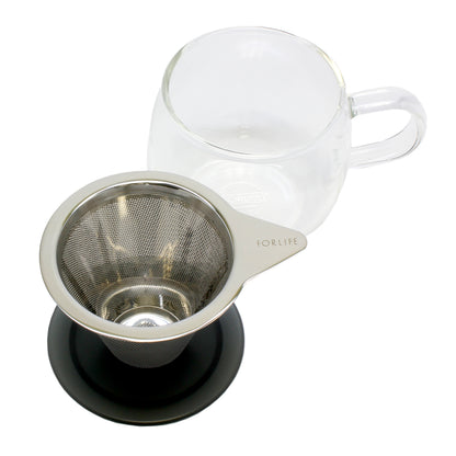 An empty strainer sits on a black lid with the mug in the background on a white background. 