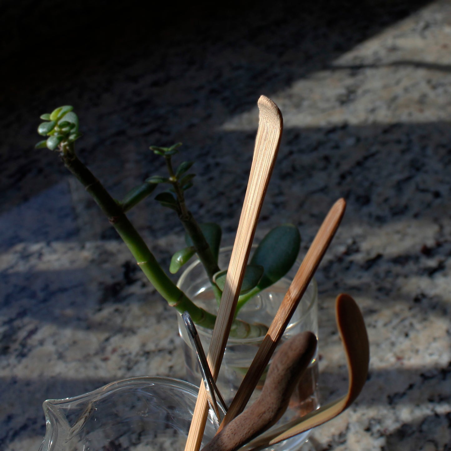Bamboo Tea Rake - with other tools in a glass pitcher, a plant in a cup is behind it on a marble surface. 