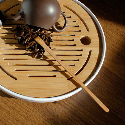 Bamboo Tea Rake - with teapot and wet leaves scooped out on a bamboo tray, a small brown tea pot is on it's side near the leaves. 