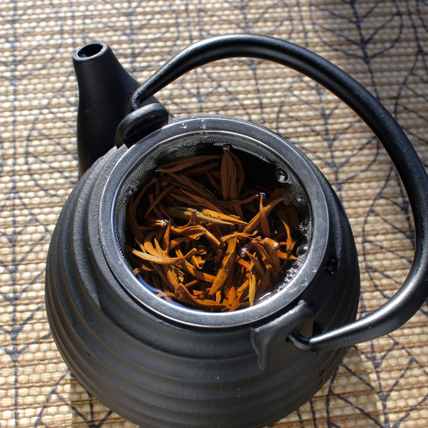 Black teapot with wet tea leaves on a leaf pattern brown table cloth.  