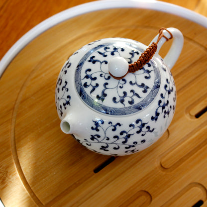 Top down view of a white ceramic teapot with blue flower and leaf patterns on a wooden surface.
