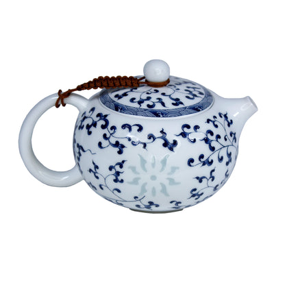 Ceramic teapot with blue floral and leaf patterns, a slightly transparent sun is on the side. A brown braided rope holds the lid to the handle. The tea pot is on a white background