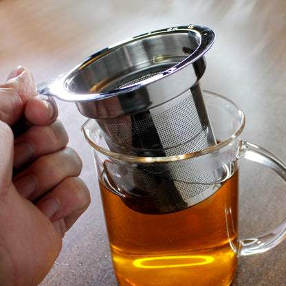 Tea strainer being lifted out of a glass pitcher on a dark wood table. 
