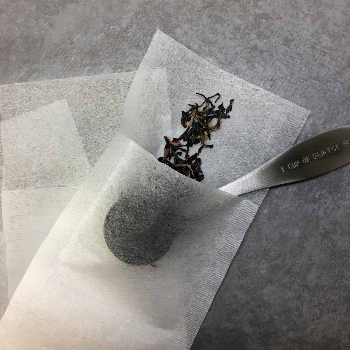 A tea scoop putting tea in the paper tea bag on a dark surface. 