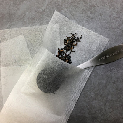 A tea scoop putting tea in the paper tea bag on a dark surface. 