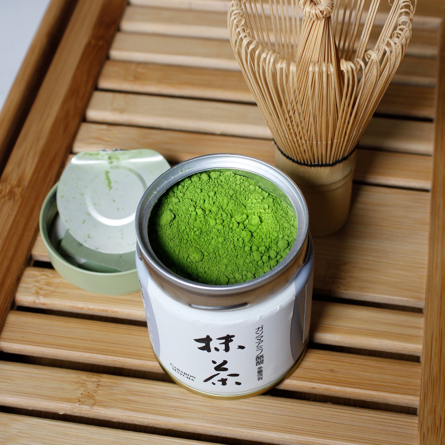 Gabaron Ceremonial Grade Matcha - Marukyu Koyamaen - Uji, Kyoto, Japan - open tin with Matcha whisk on a bamboo tray, time lid next to open container. Tasting Notes:
nori • wheat grass • unsweetened cocoa