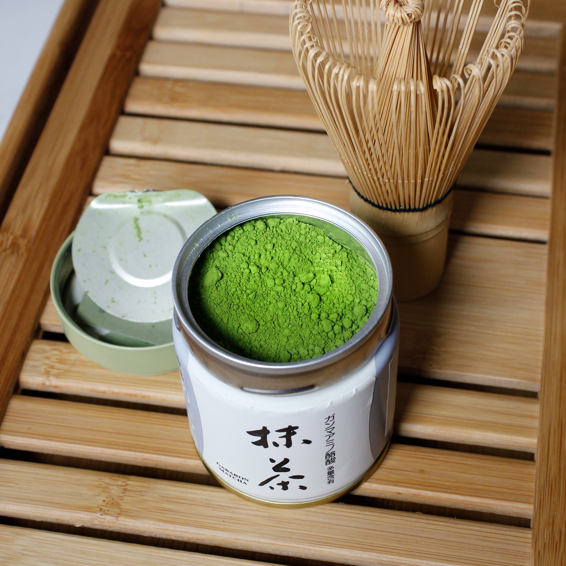 Gabaron Ceremonial Grade Matcha - Marukyu Koyamaen - Uji, Kyoto, Japan - open tin with Matcha whisk on a bamboo tray, time lid next to open container. Tasting Notes:
nori • wheat grass • unsweetened cocoa
