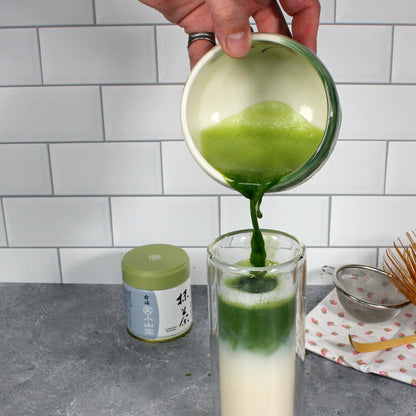 Gabaron Ceremonial Grade Matcha - Marukyu Koyamaen - Uji, Kyoto, Japan - latte, the matcha is being poured into a tall glass of milk. A tin, sifter, scoop and whisk are on the counter. Tasting Notes:
nori • wheat grass • unsweetened cocoa 