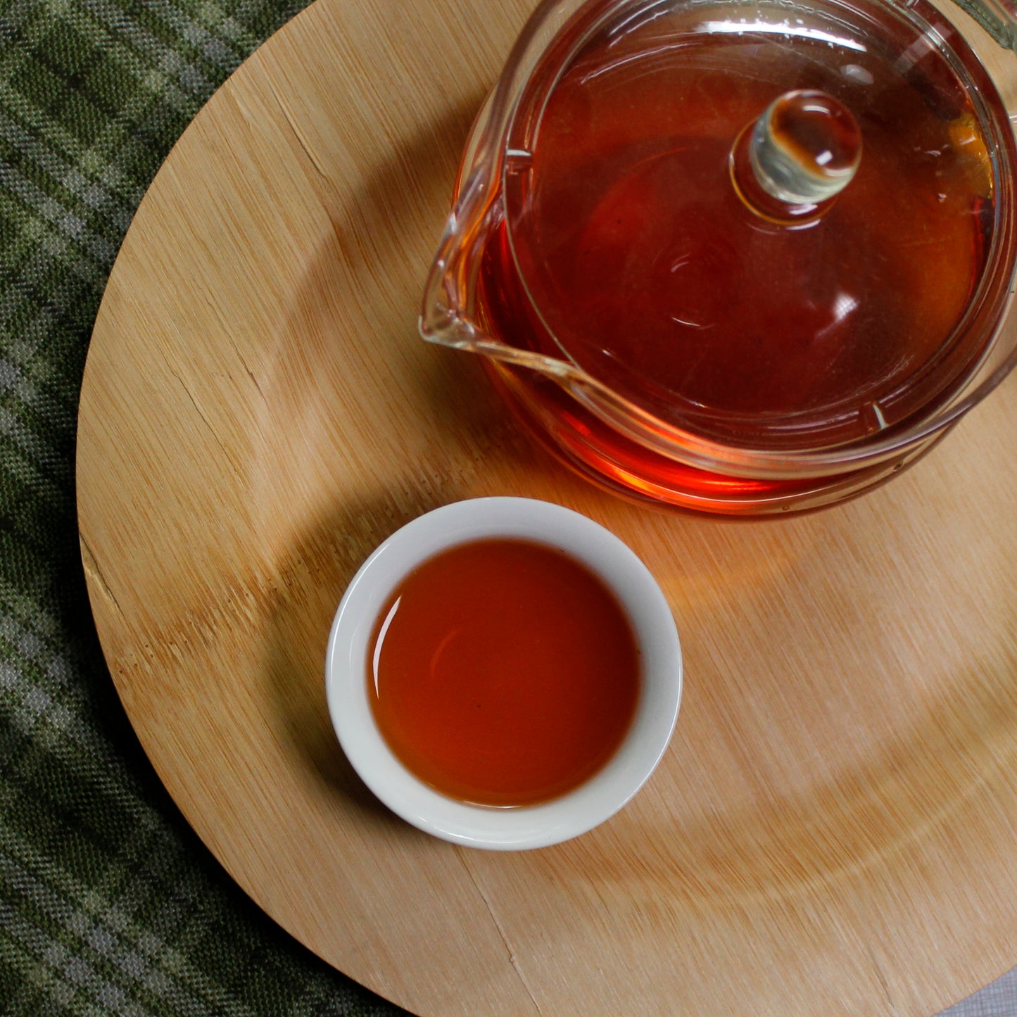 Down shot of a full glass tea pot and cup on a bamboo tray on a cloth background. 