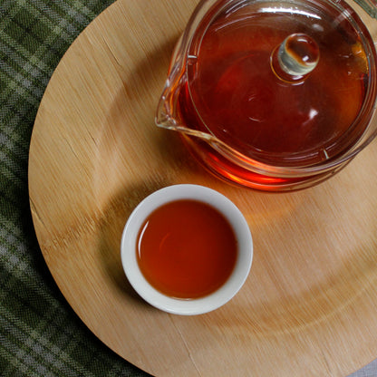 Down shot of a full glass tea pot and cup on a bamboo tray on a cloth background. 