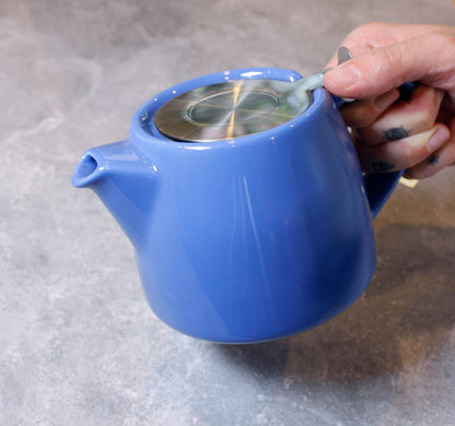 Blue teapot with a metal flip top held by a hand on a gray background