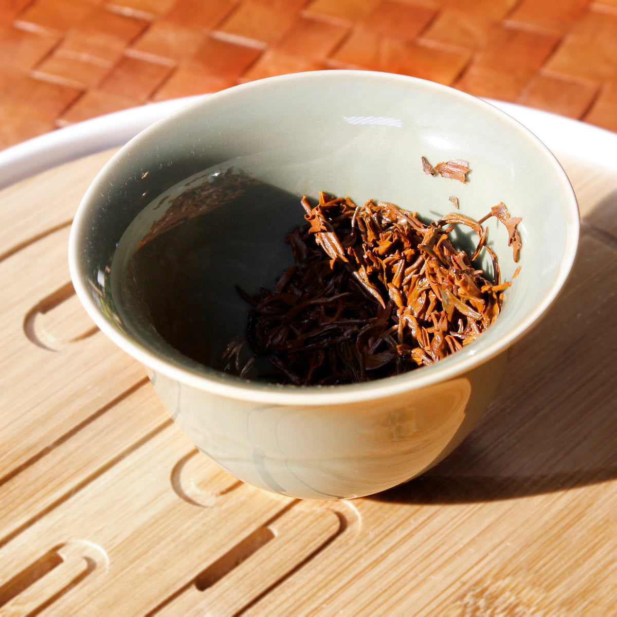 Wet leaves in a green gaiwan on a bamboo tray. 