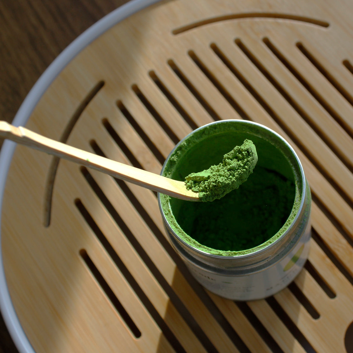 Bamboo Matcha Scoop - Chashaku - with matcha being scooped out of a canister on a bamboo tray. 