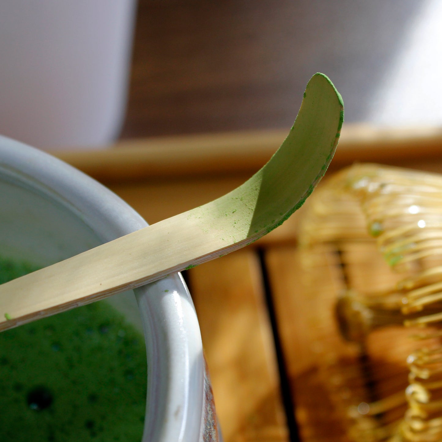 Bamboo Matcha Scoop - Chashaku - used laying on a matcha bowl with a matcha whisk and tray in the background. 