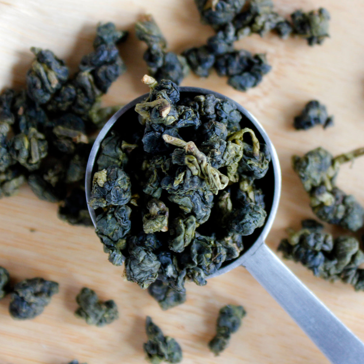 Tea scoop filled with round tea leaves, more tea is on the background.