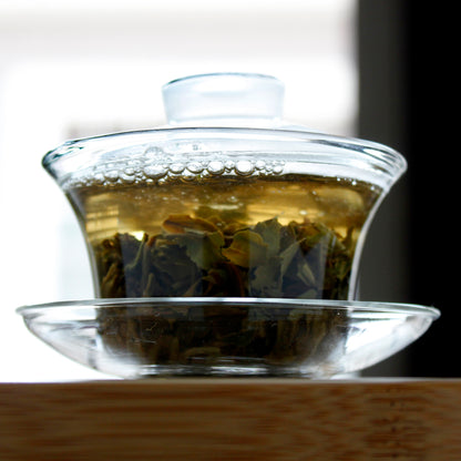 Gaiwan with tea and leaves, the water starting to turn a warm brown from the tea.