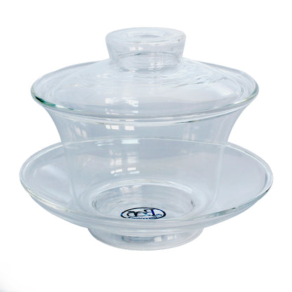 A clear glass gaiwan, which is a type of teaware commonly used for steeping tea, consisting of a bowl with a lid on top, placed on a matching saucer.