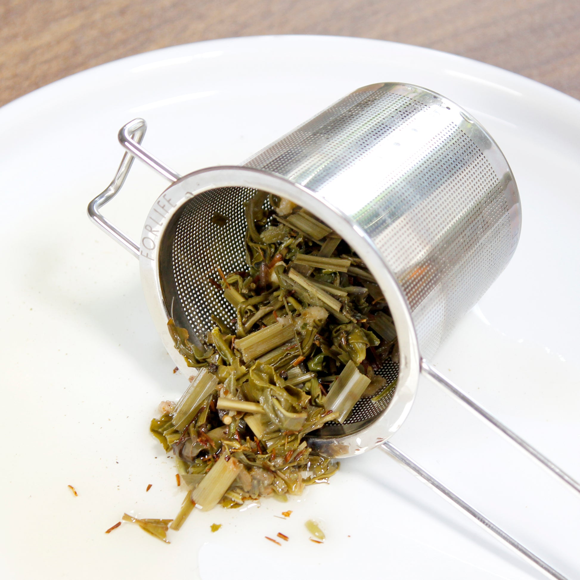The strainer on its side, wet tea leaves spilling out on a dish. 