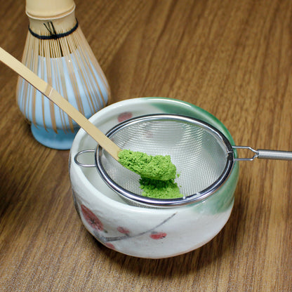 Yugen Ceremonial Grade Matcha - Marukyu Koyamaen - Uji, Kyoto, Japan - powder in a Matcha shifter over a Matcha bowl, whisk in the back. Tasting Notes:
broccoli • asparagus • white bean