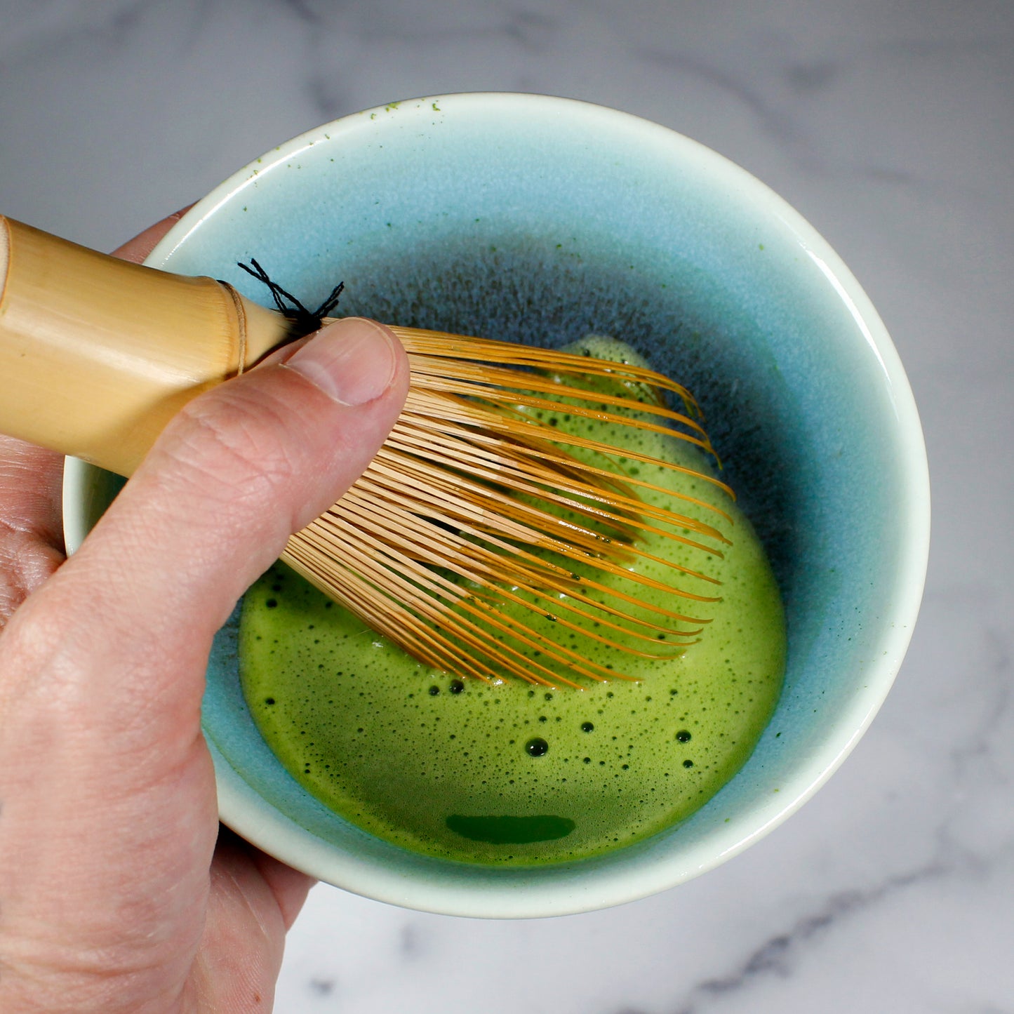 Yugen Ceremonial Grade Matcha - Marukyu Koyamaen - Uji, Kyoto, Japan - whisked in a Matcha bowl, handle holding a whisk. Tasting Notes:
broccoli • asparagus • white bean